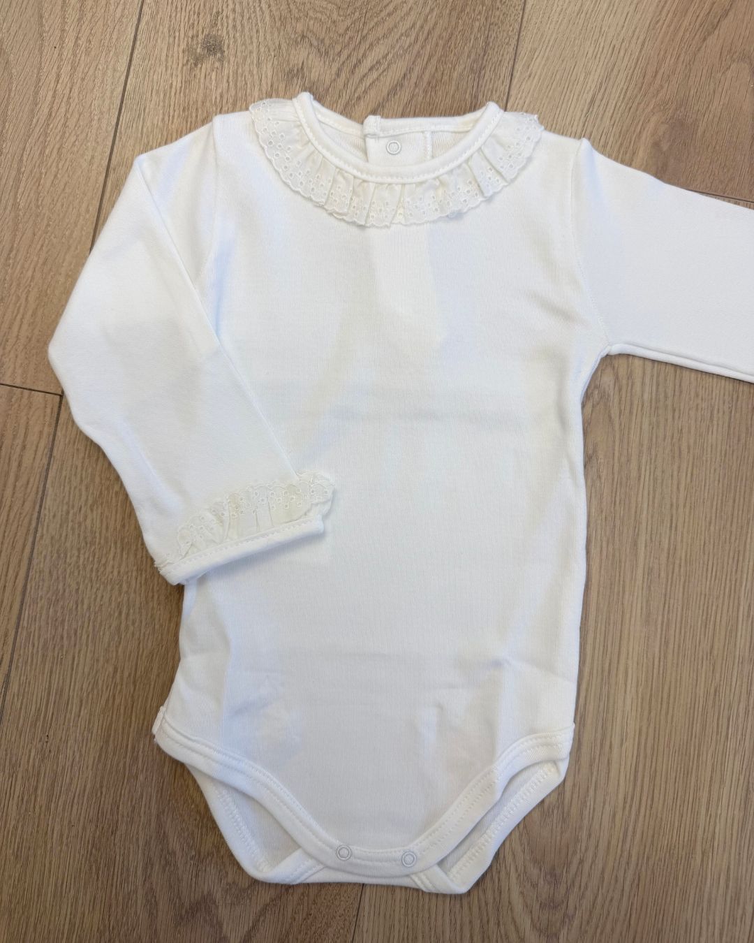 Calamaro long sleeve baby girls vest in white and ivory with a delicate broderie anglaise lace frill collar, matching frilled cuffs and popper fastenings.