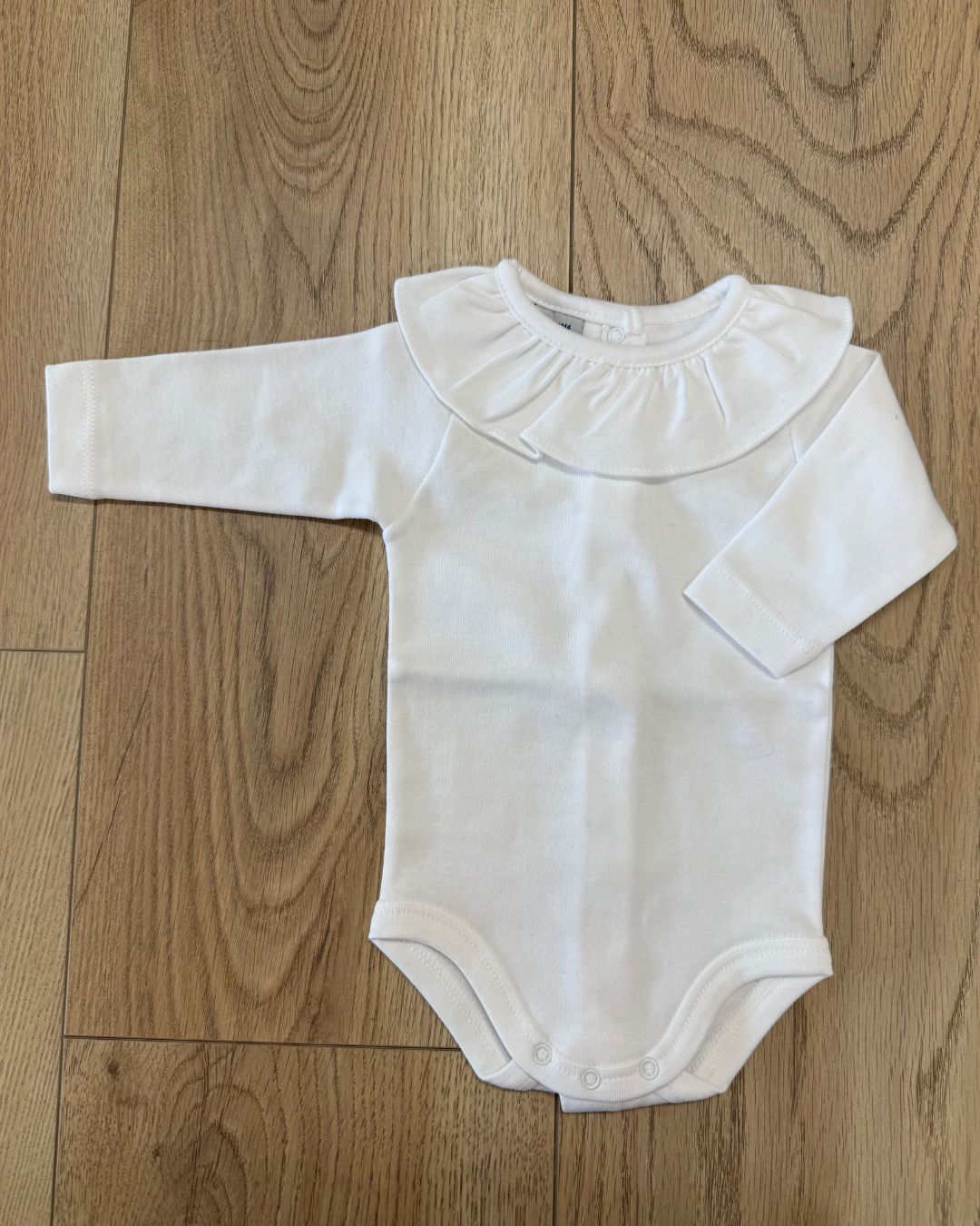 Babidu white baby girls long sleeve cotton bodysuit with ruffle neckline.