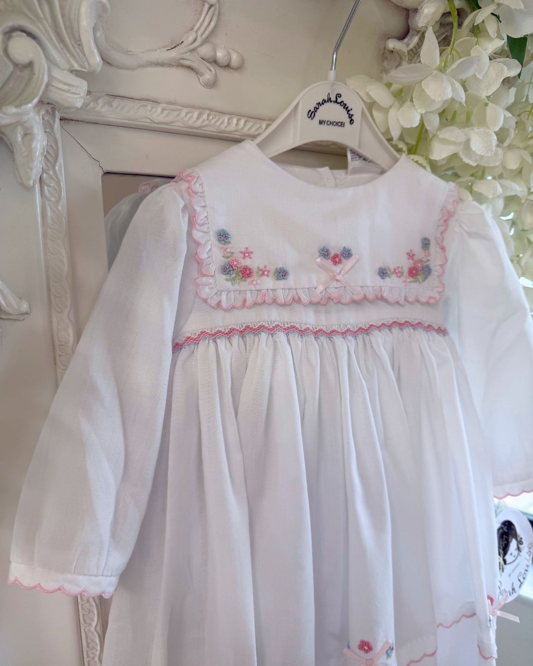 Sarah Louise Evelyn white girls smocked dress with pink and blue floral embroidery, square frill collar, satin bows and bow back tie.