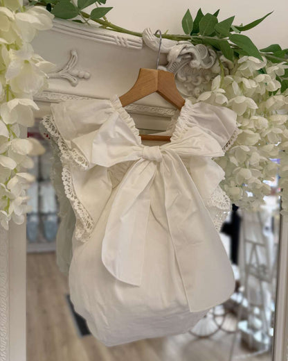 Phi Ivy Bow Back Romper featuring soft ivory cotton, lace-trimmed frill sleeves and an oversized statement bow at the back.