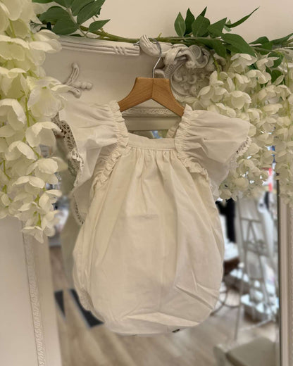 Phi Ivy Bow Back Romper featuring soft ivory cotton, lace-trimmed frill sleeves and an oversized statement bow at the back.