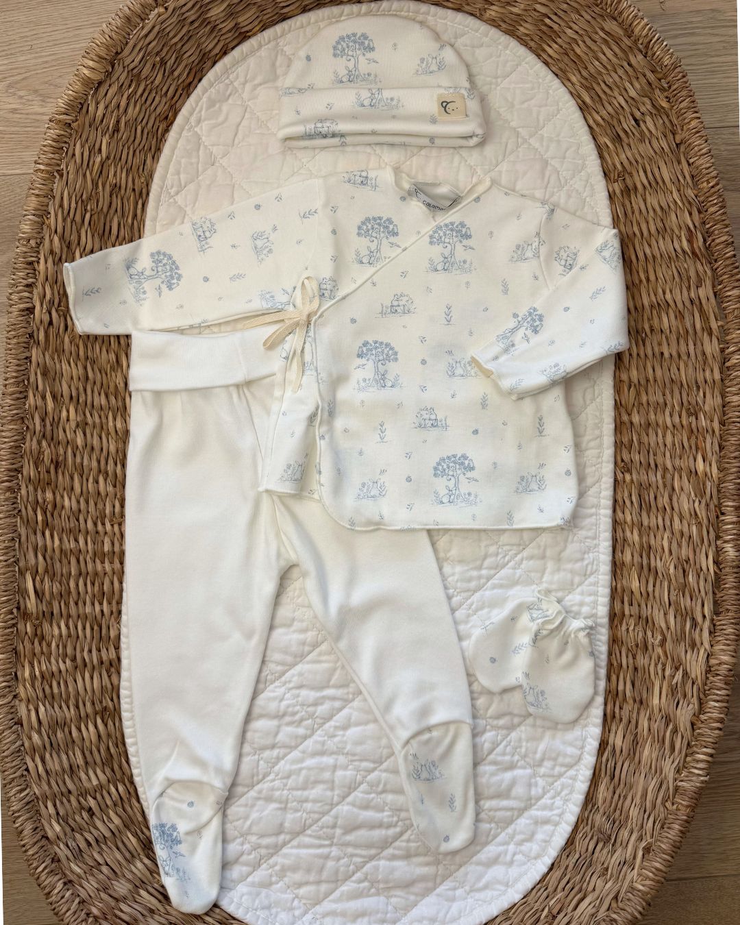 Calamaro Mon Cheri four-piece newborn baby gift set in ivory with pink or blue woodland print, featuring a wrap top, footed trousers, matching hat and scratch mittens.
