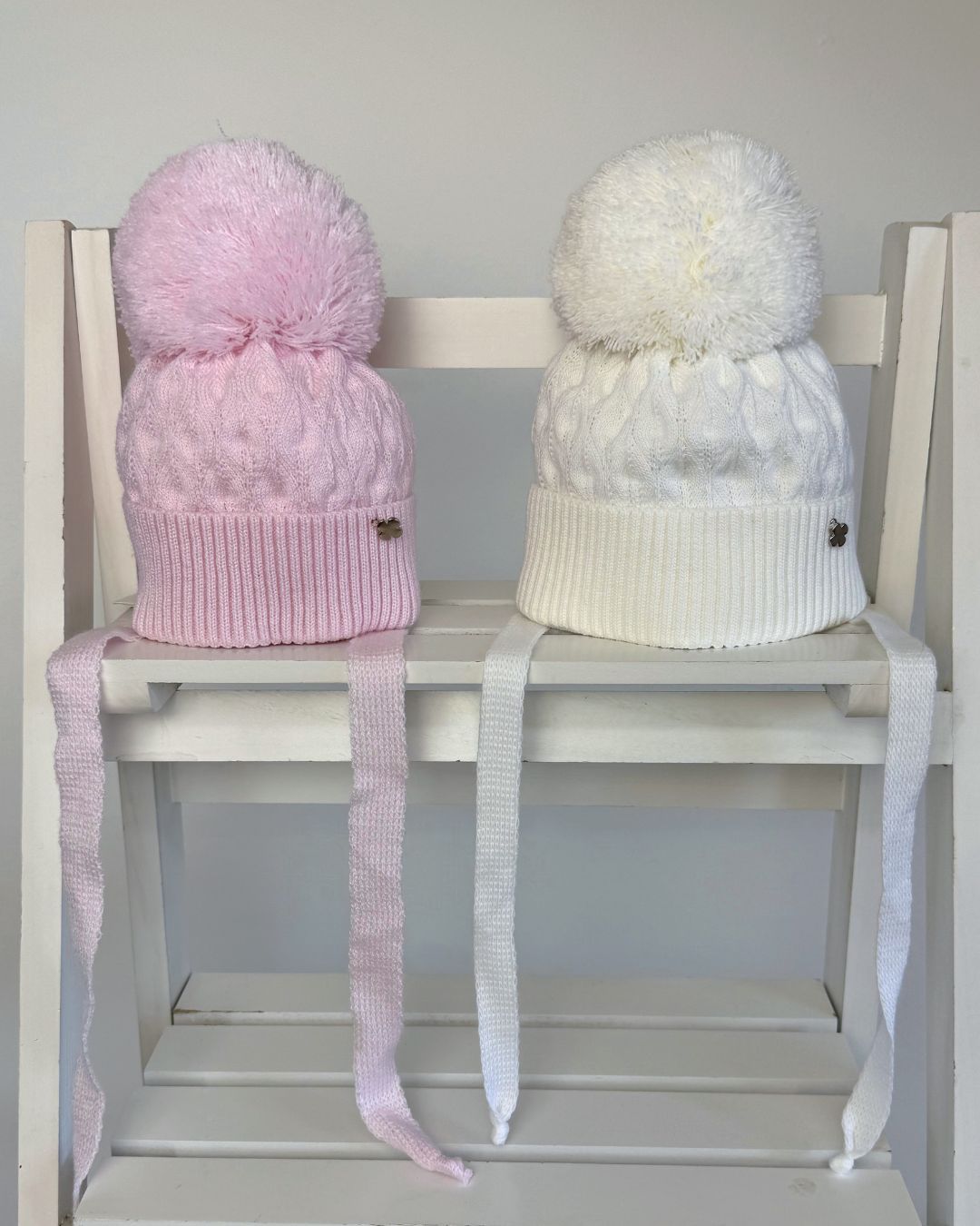 Jamiks Belinda cable knit baby pom hat with chin ties, available in soft pink and white.