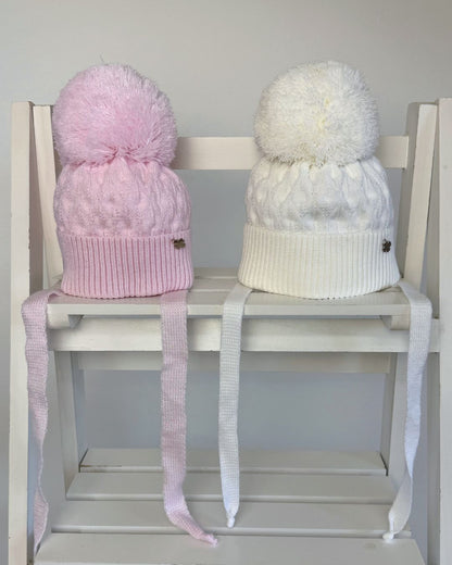 Jamiks Belinda cable knit baby pom hat with chin ties, available in soft pink and white.