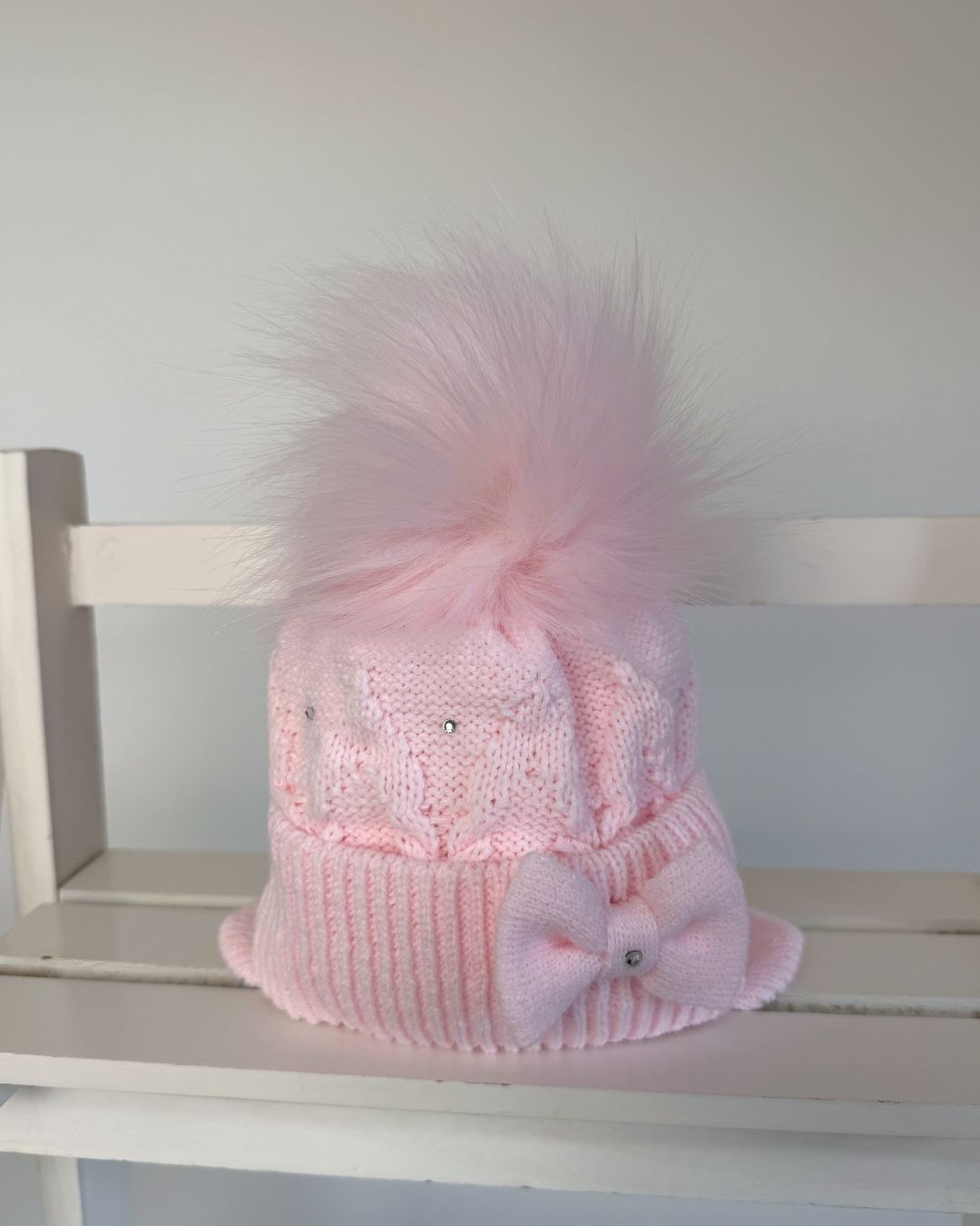 Little Nosh pink knitted girls’ winter hat with faux fur pom pom, bow, diamanté detailing and ear covers.