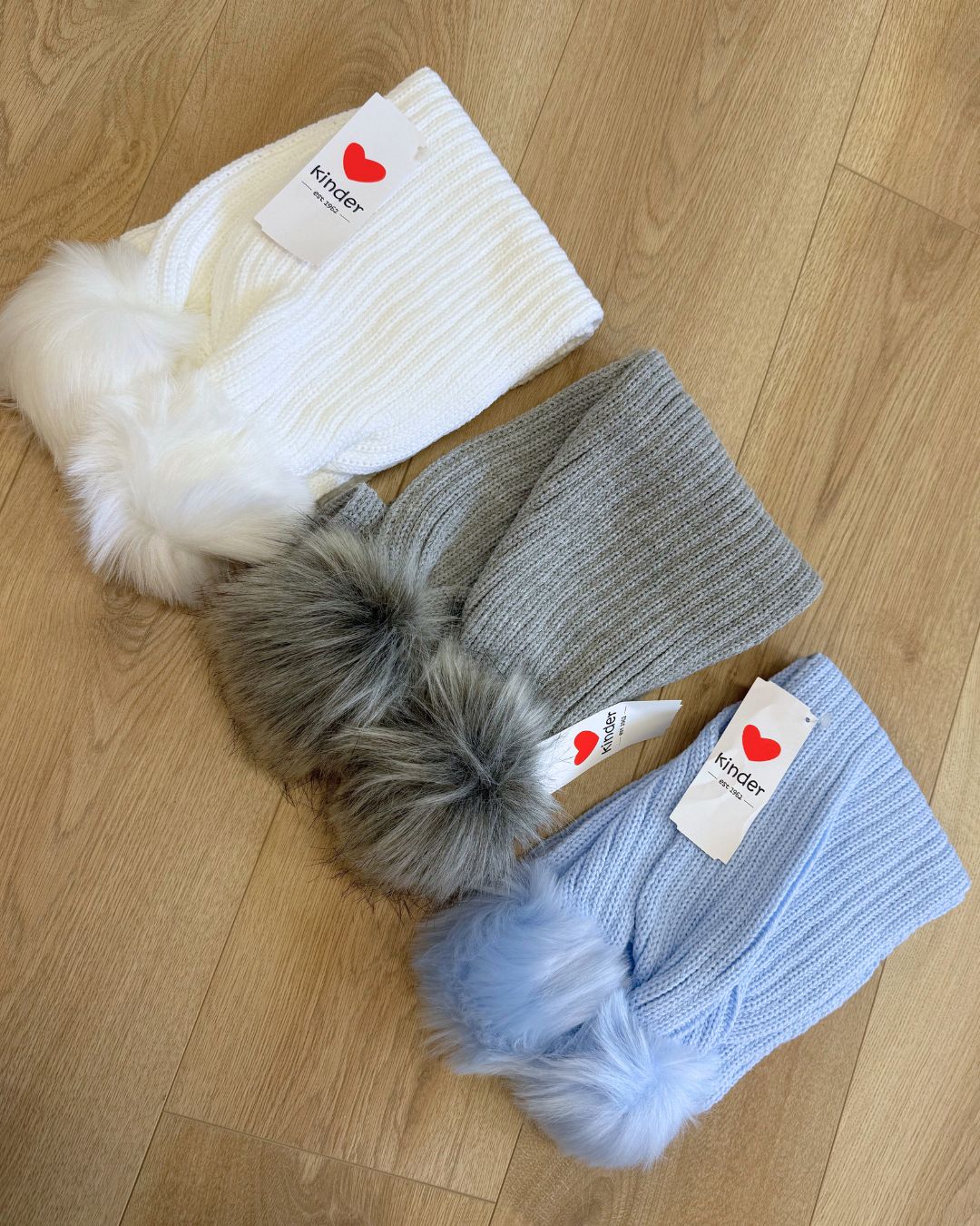 Kinder knitted children's winter scarves with faux fur pom poms in white, grey and baby blue.