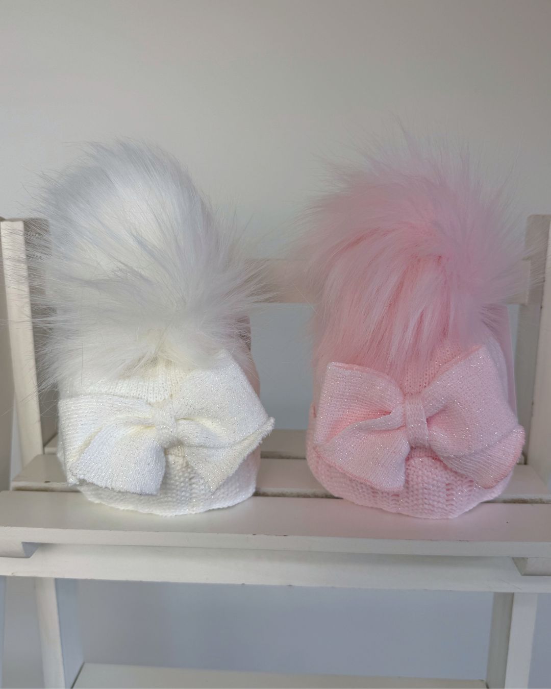 Little Nosh baby girls sparkle knit winter hat in white or pink with faux fur pom pom, oversized side bow and scalloped trim.