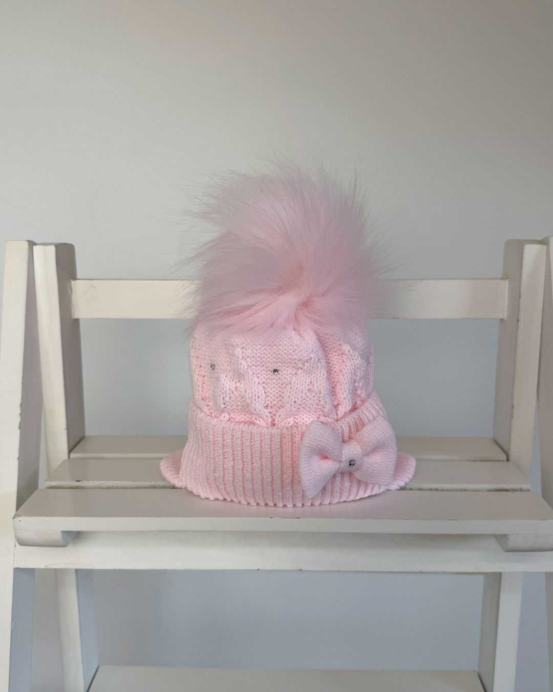 Little Nosh pink knitted girls’ winter hat with faux fur pom pom, bow, diamanté detailing and ear covers.