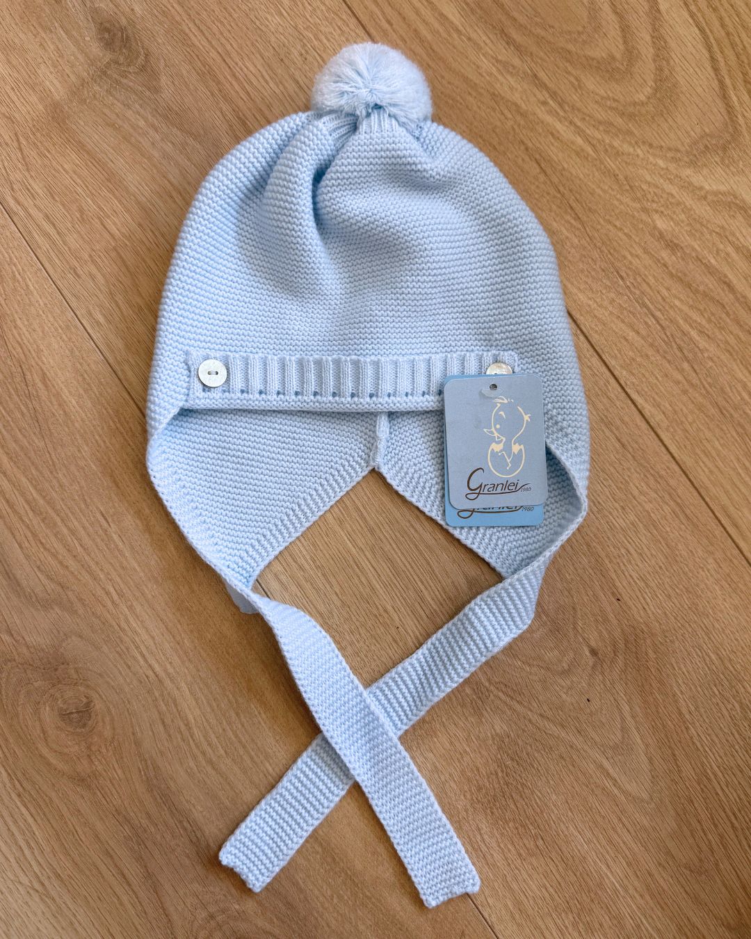 Granlei celeste blue knitted baby boys pom hat with ties and button detailing.