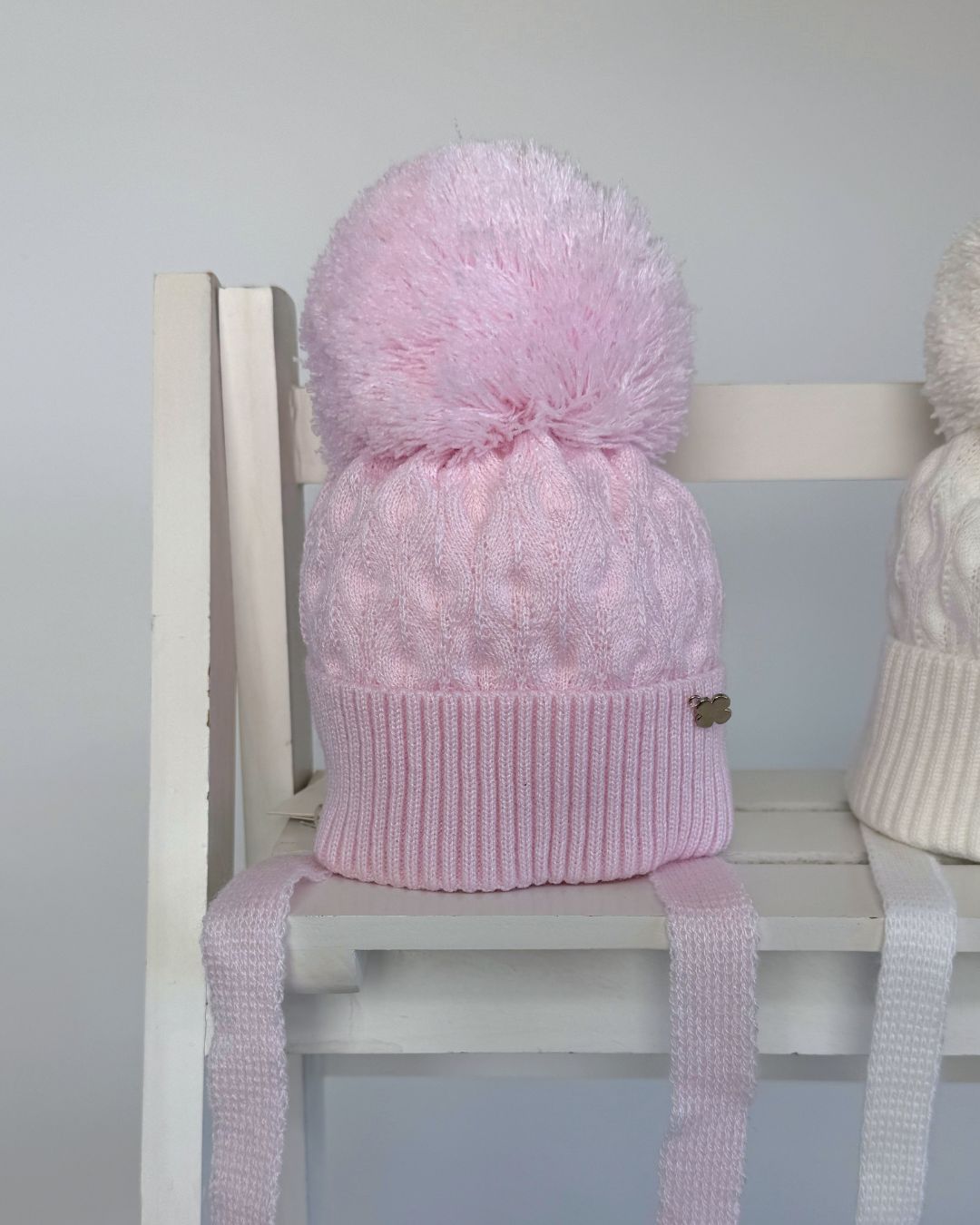 Jamiks Belinda cable knit baby pom hat with chin ties, available in soft pink and white.