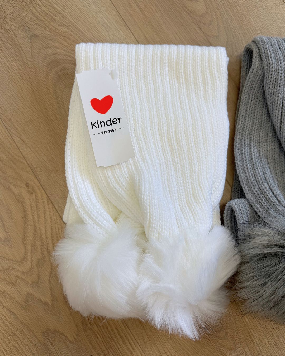 Kinder knitted children's winter scarves with faux fur pom poms in white, grey and baby blue.
