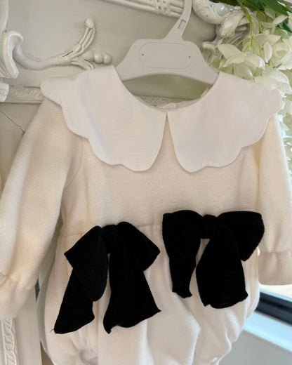 Phi Estelle ivory knitted baby girls romper with white scalloped collar and black bows.