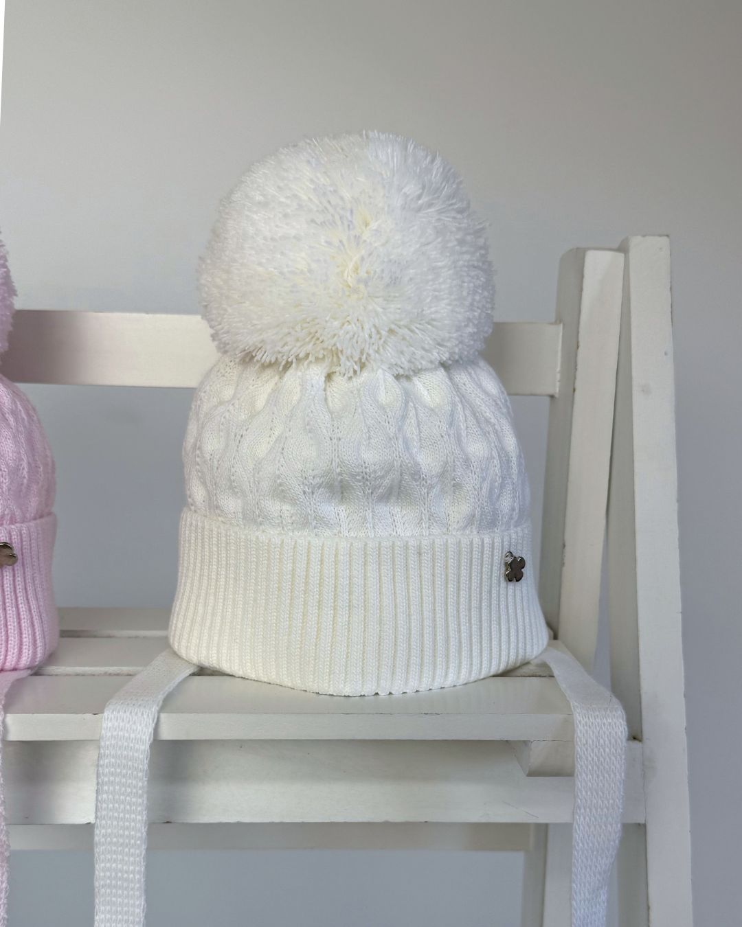 Jamiks Belinda cable knit baby pom hat with chin ties, available in soft pink and white.