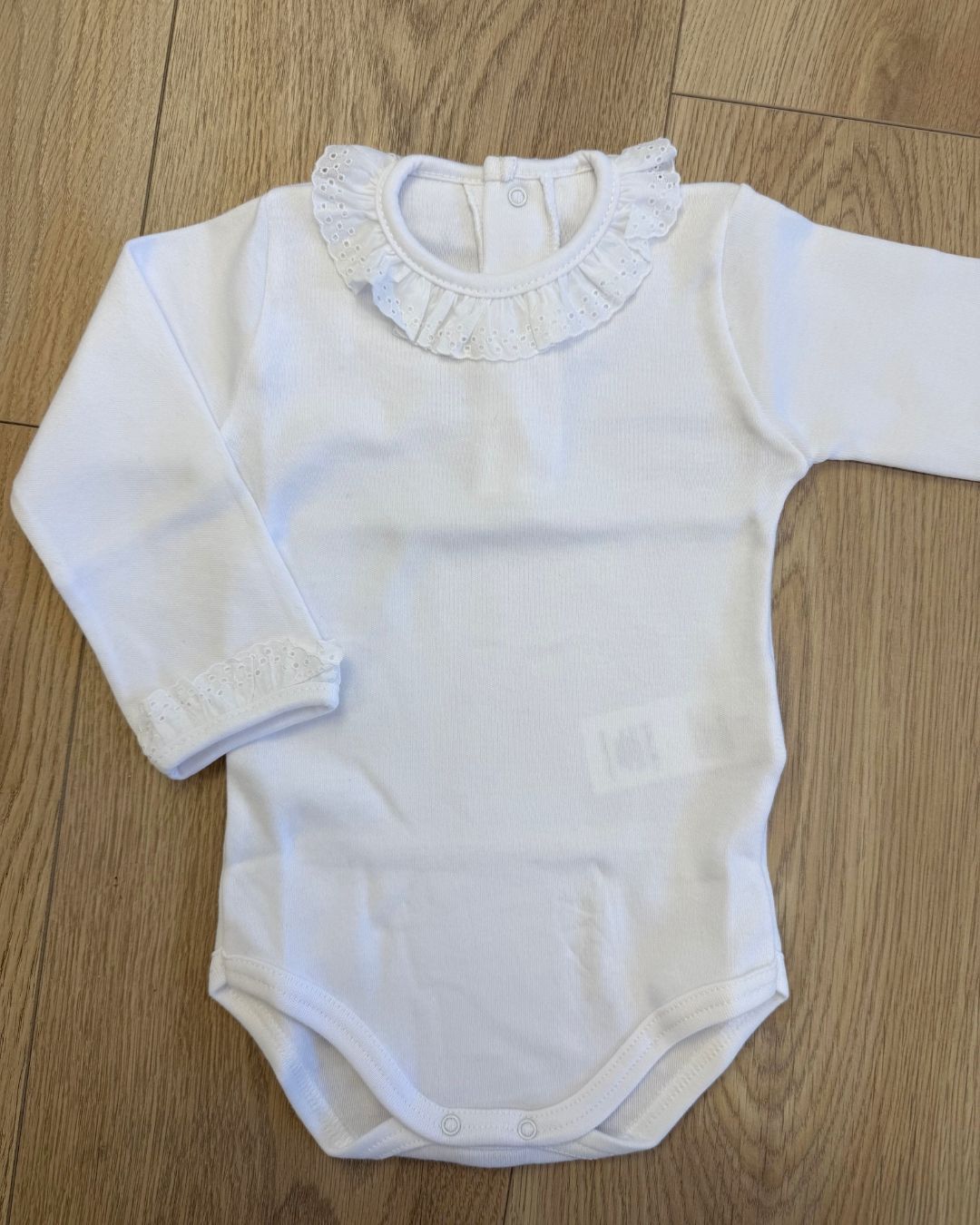 Calamaro long sleeve baby girls vest in white and ivory with a delicate broderie anglaise lace frill collar, matching frilled cuffs and popper fastenings.