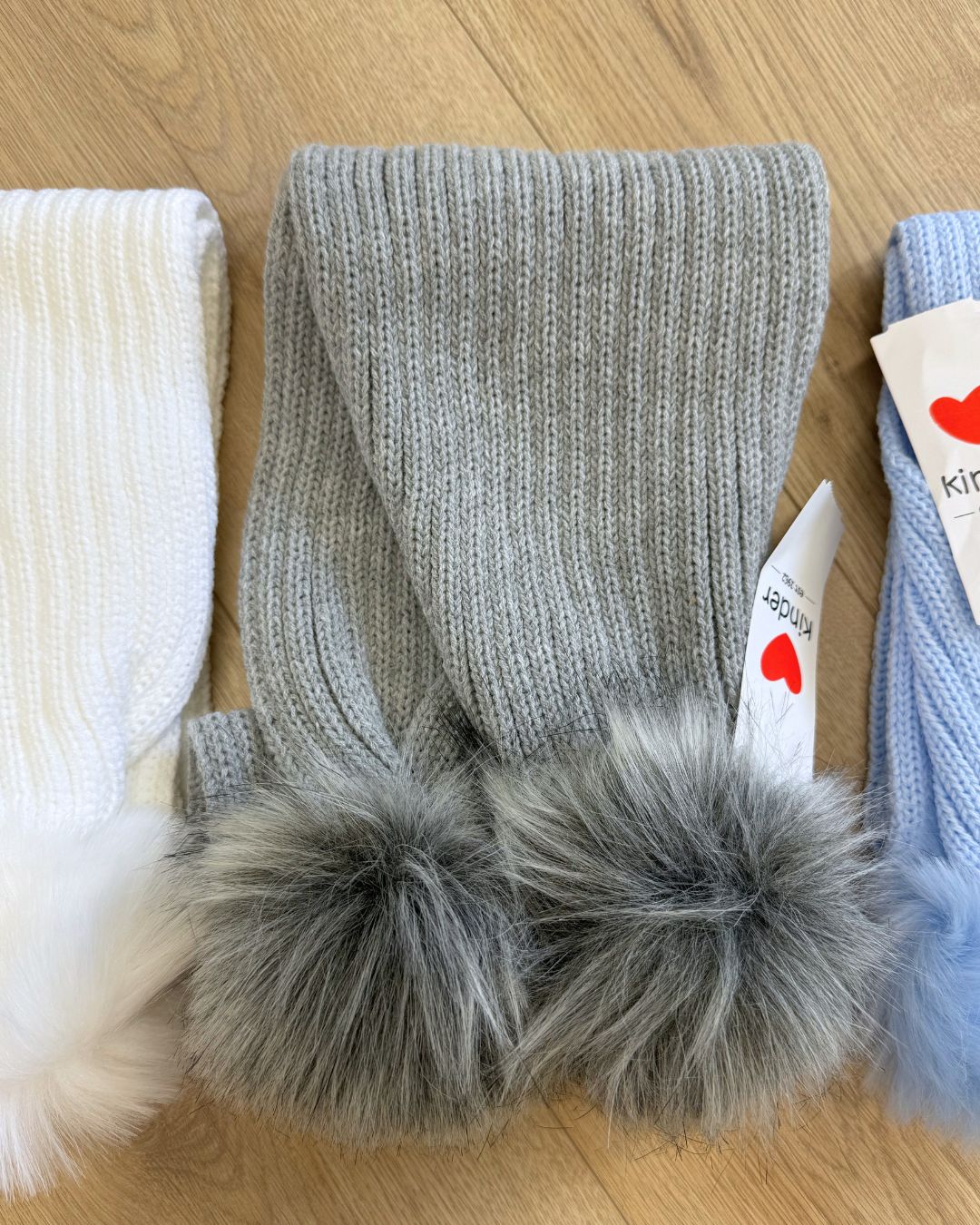 Kinder knitted children's winter scarves with faux fur pom poms in white, grey and baby blue.