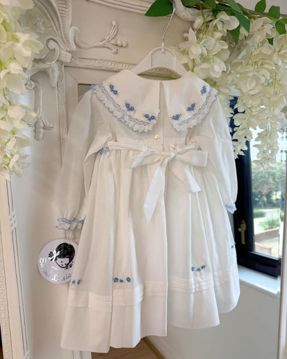 Sarah Louise Eleanor ivory girls smocked dress with blue floral embroidery, frilled collar, long sleeves and bow back tie.