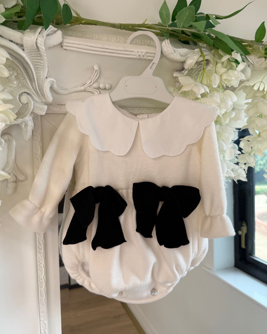 Phi Estelle ivory knitted baby girls romper with white scalloped collar and black bows.