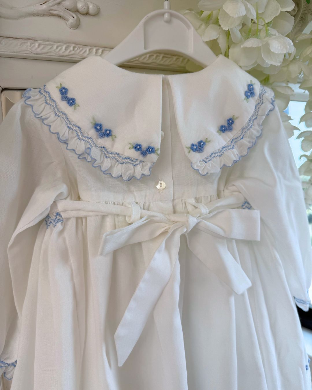 Sarah Louise Eleanor ivory girls smocked dress with blue floral embroidery, frilled collar, long sleeves and bow back tie.