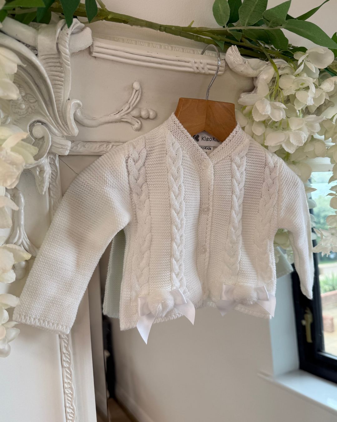 Girls white knitted cardigan with cable knit detailing, satin bows and pom poms.