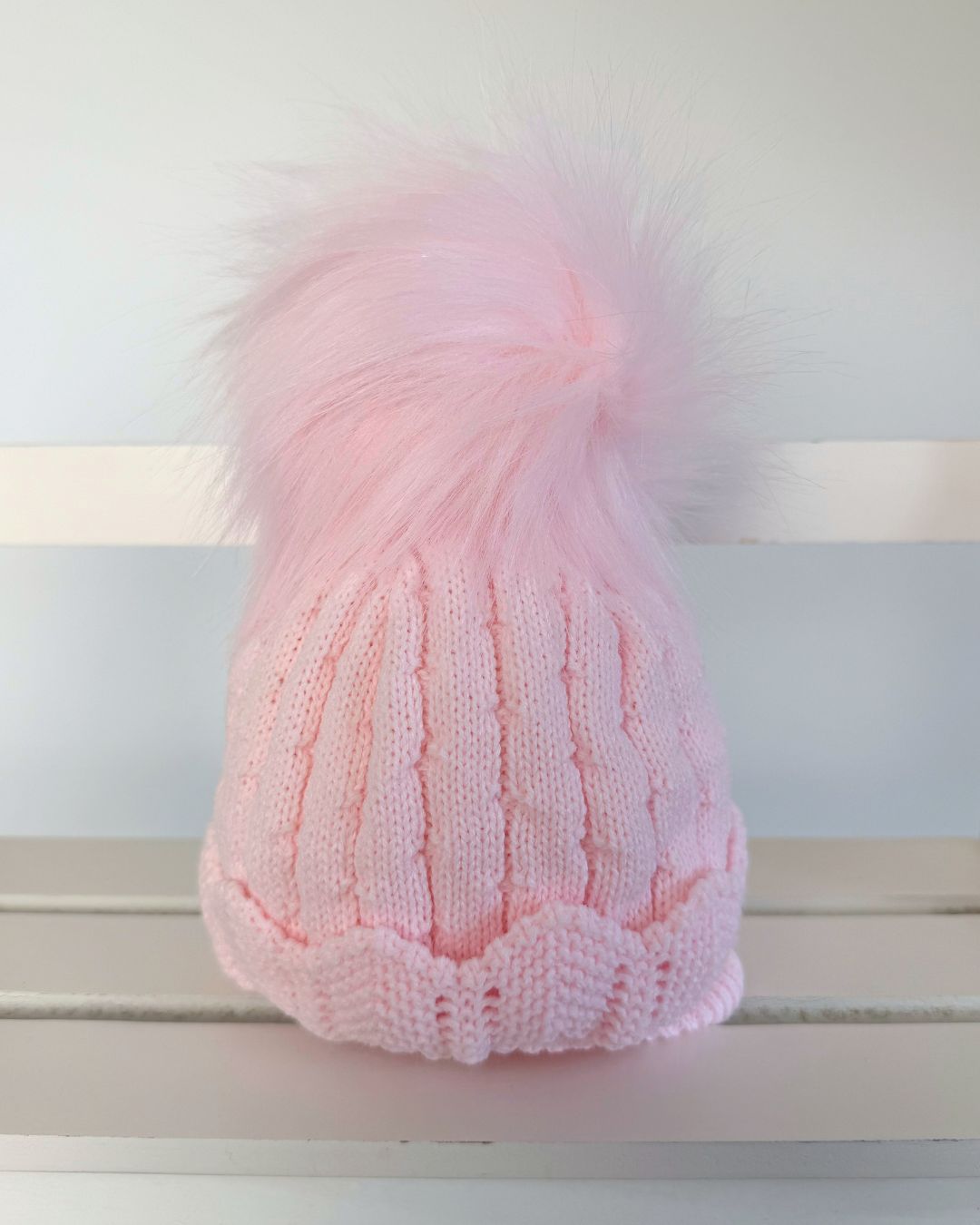 Little Nosh Aurora pink knitted baby girls winter hat with faux fur pom pom, scalloped hem and cosy ear covers.