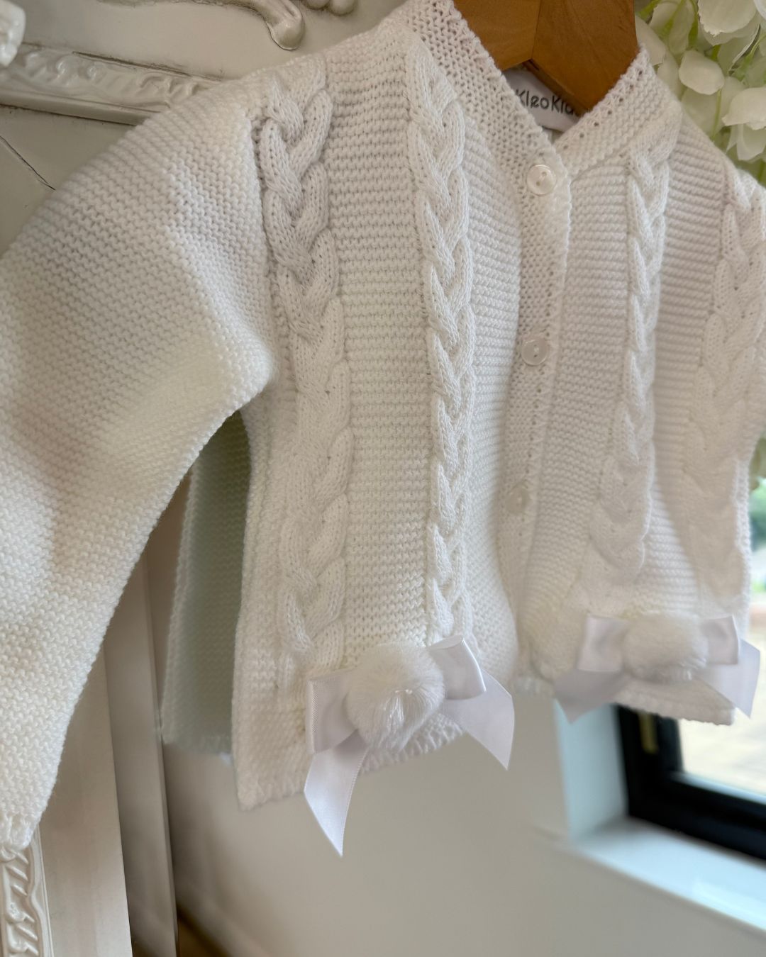 Girls white knitted cardigan with cable knit detailing, satin bows and pom poms.