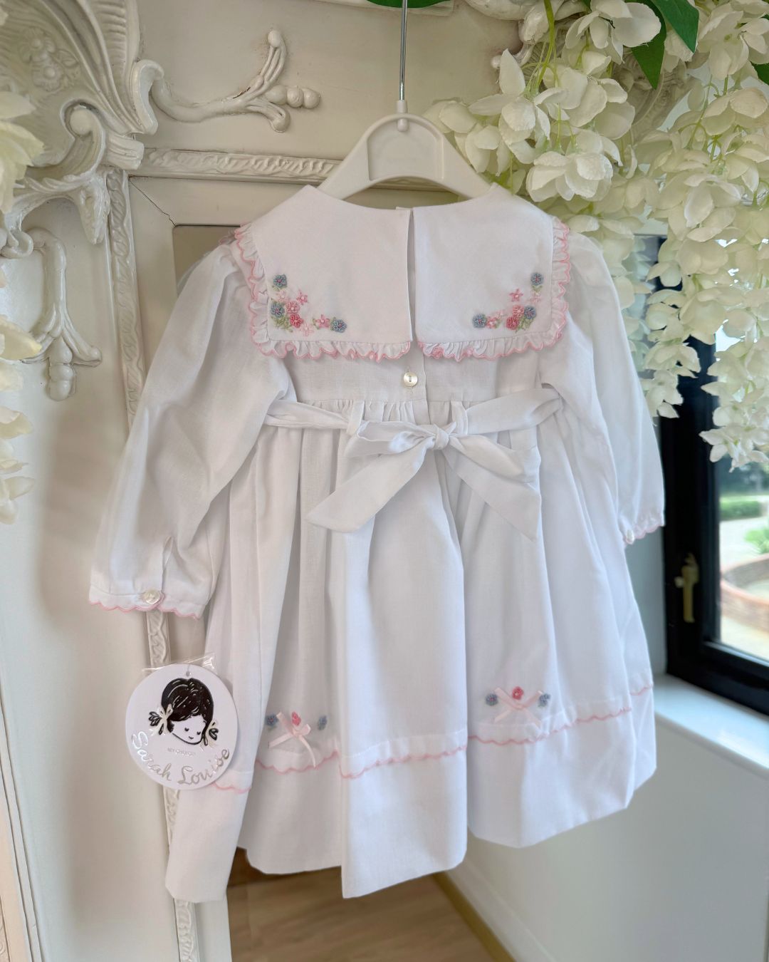 Sarah Louise Evelyn white girls smocked dress with pink and blue floral embroidery, square frill collar, satin bows and bow back tie.