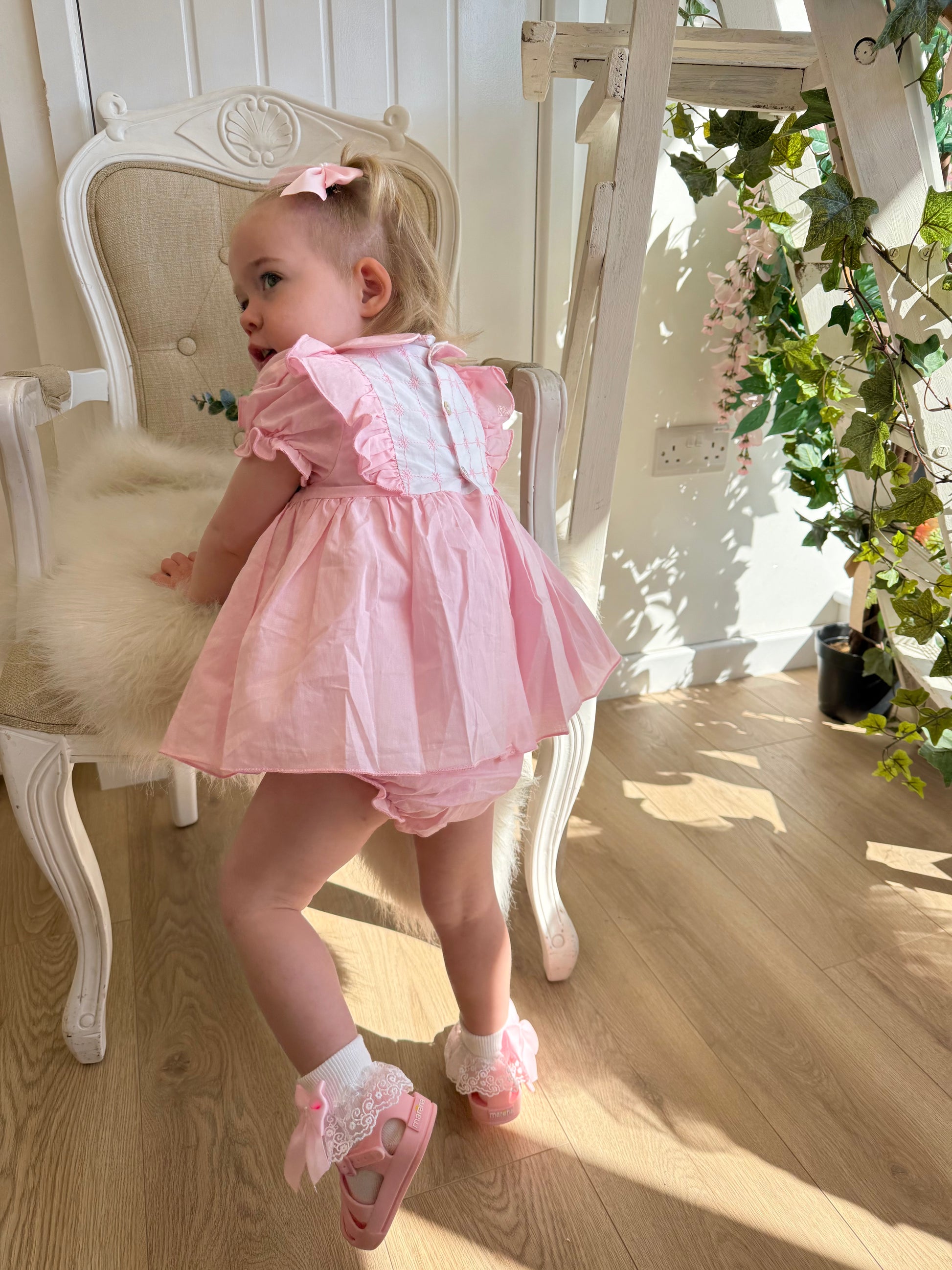 A soft rosy pink, this traditional Spanish-style dress is paired with matching jam pants. Adorned with a white chest panel featuring subtle stitch detailing, the dress is finished with pretty shoulder frills, two bow accents and a classic Peter Pan collar.