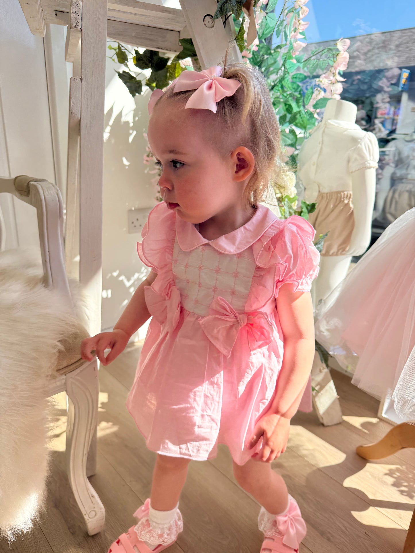 A soft rosy pink, this traditional Spanish-style dress is paired with matching jam pants. Adorned with a white chest panel featuring subtle stitch detailing, the dress is finished with pretty shoulder frills, two bow accents and a classic Peter Pan collar.