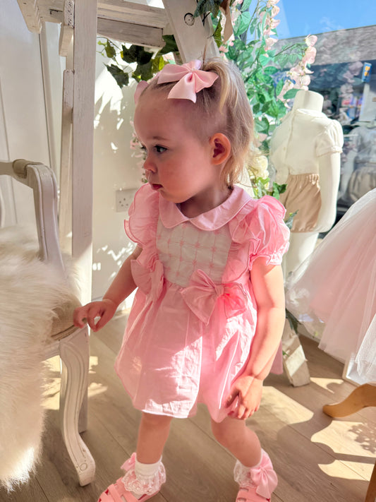 A soft rosy pink, this traditional Spanish-style dress is paired with matching jam pants. Adorned with a white chest panel featuring subtle stitch detailing, the dress is finished with pretty shoulder frills, two bow accents and a classic Peter Pan collar.