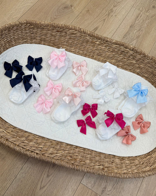 Crafted in soft white fabric, each pair features a delicate lace frill trim, finished with a pretty satin side bow and elegant pearl chain centre.