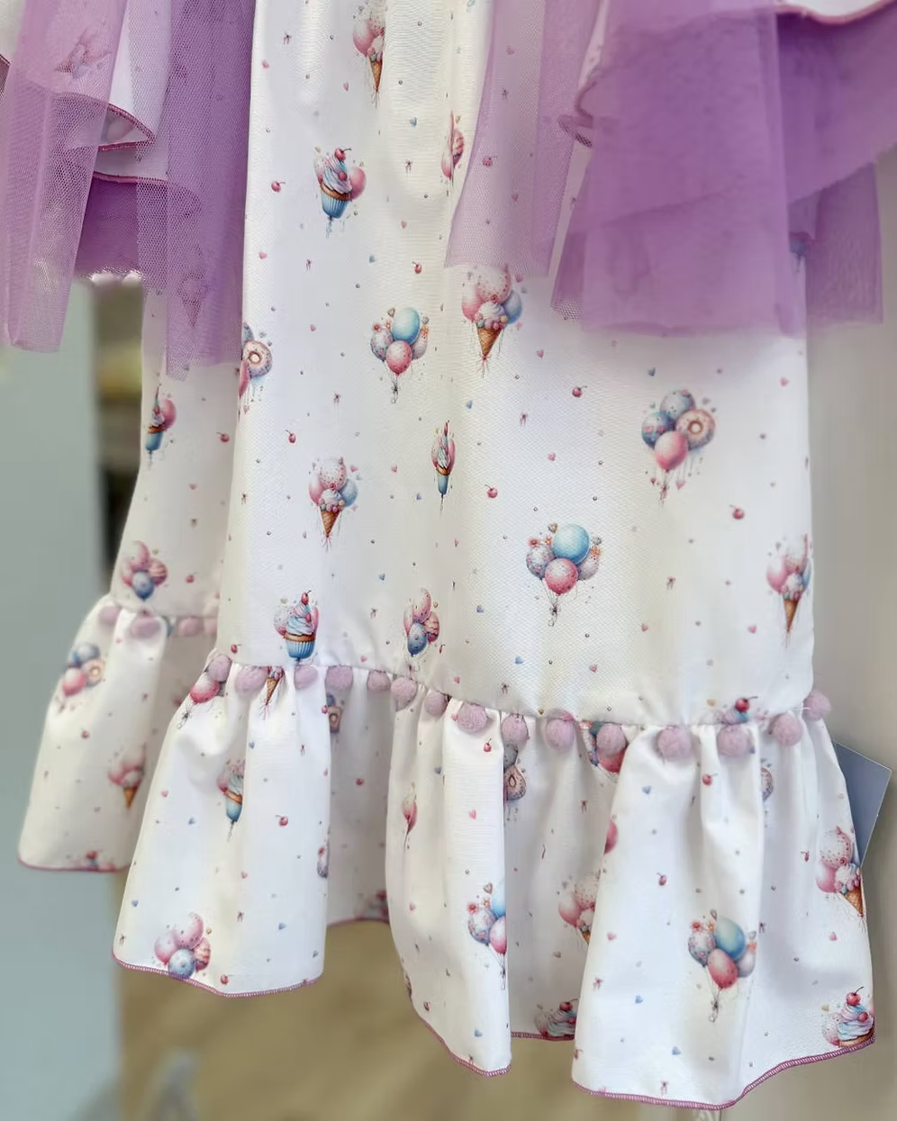 Babine Lilac Dream Dress featuring an ice cream, balloon and cupcake print, lilac tulle bows, frill sleeves, pom pom hem trim and scoop back tie.