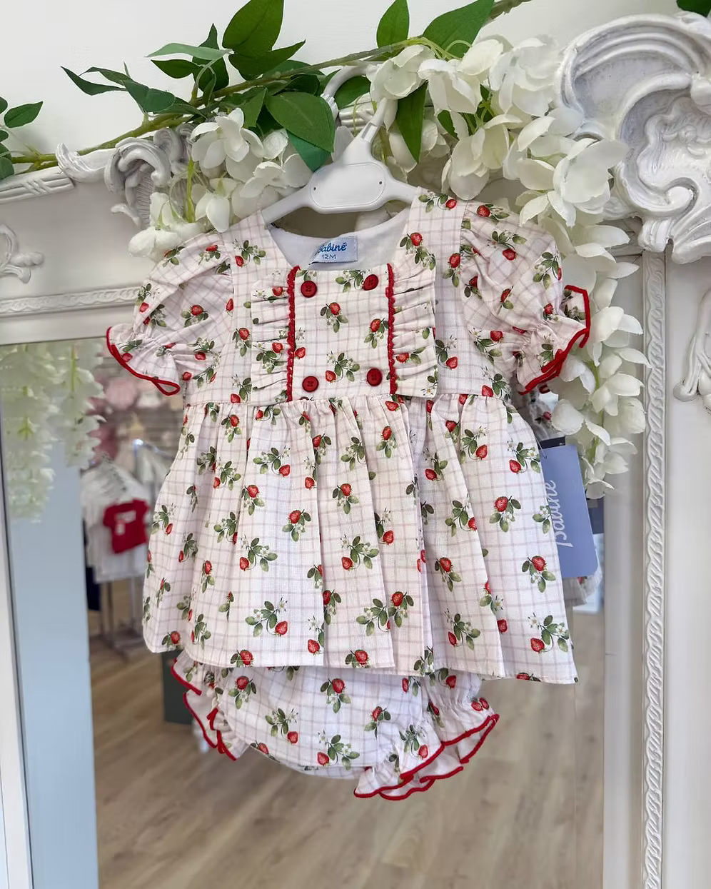 Off-white and pink check baby dress with strawberry print, frill chest detail, puff sleeves, red stitch trims, matching pants, and bow back fastening.