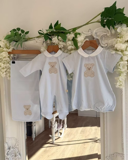 Baby Gi Teddy Shawl featuring soft cotton fabric, embroidered teddy bear detail and available in ivory, pink and blue colourways. Along side matching babygrow and romper.