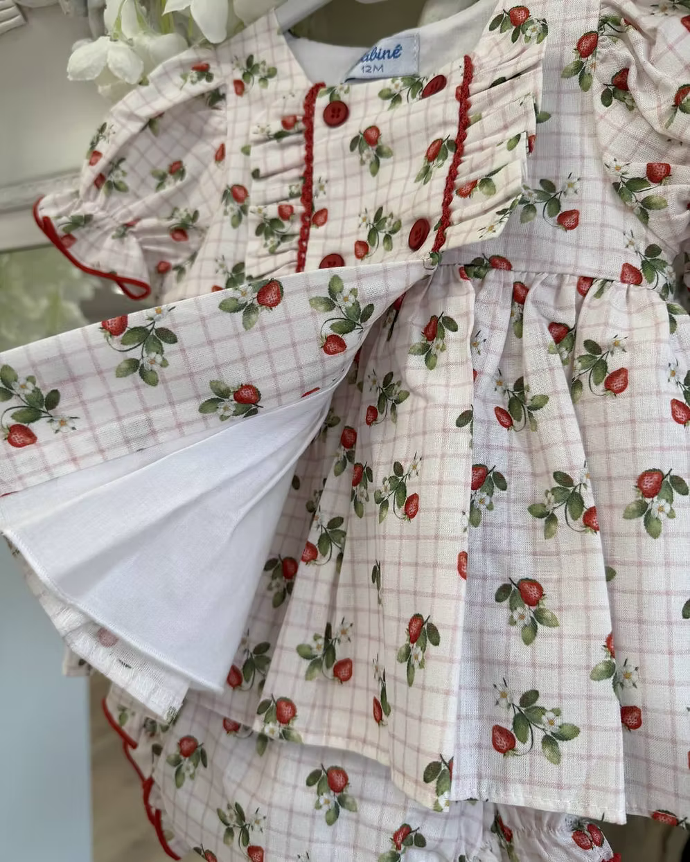 Off-white and pink check baby dress with strawberry print, frill chest detail, puff sleeves, red stitch trims, matching pants, and bow back fastening.