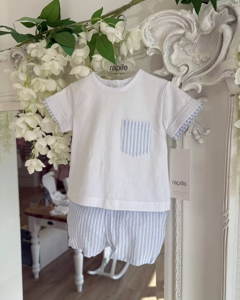 Children's white shirt with a blue striped pocket and striped shorts hanging on a decorative mirror.