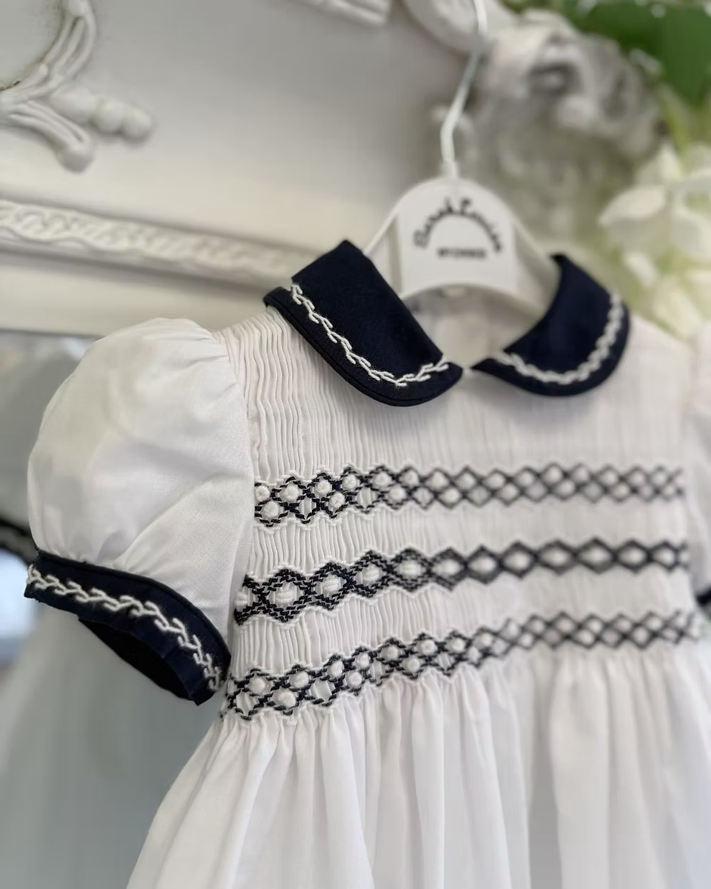 white romper fully smocked chest with a navy Peter Pan collar and sleeve trim with white feather stitch detailing.