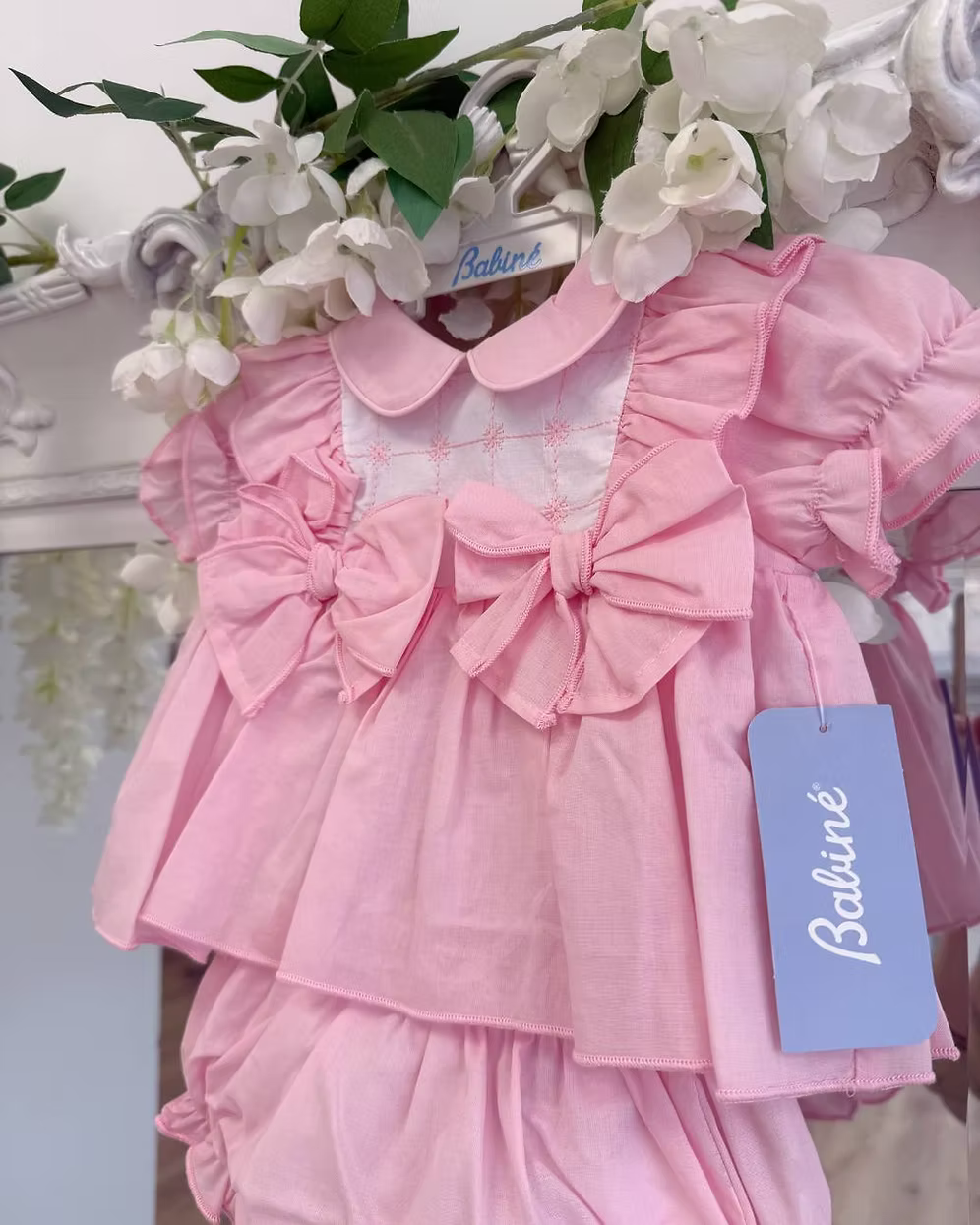 A soft rosy pink, this traditional Spanish-style dress is paired with matching jam pants. Adorned with a white chest panel featuring subtle stitch detailing, the dress is finished with pretty shoulder frills, two bow accents and a classic Peter Pan collar.
