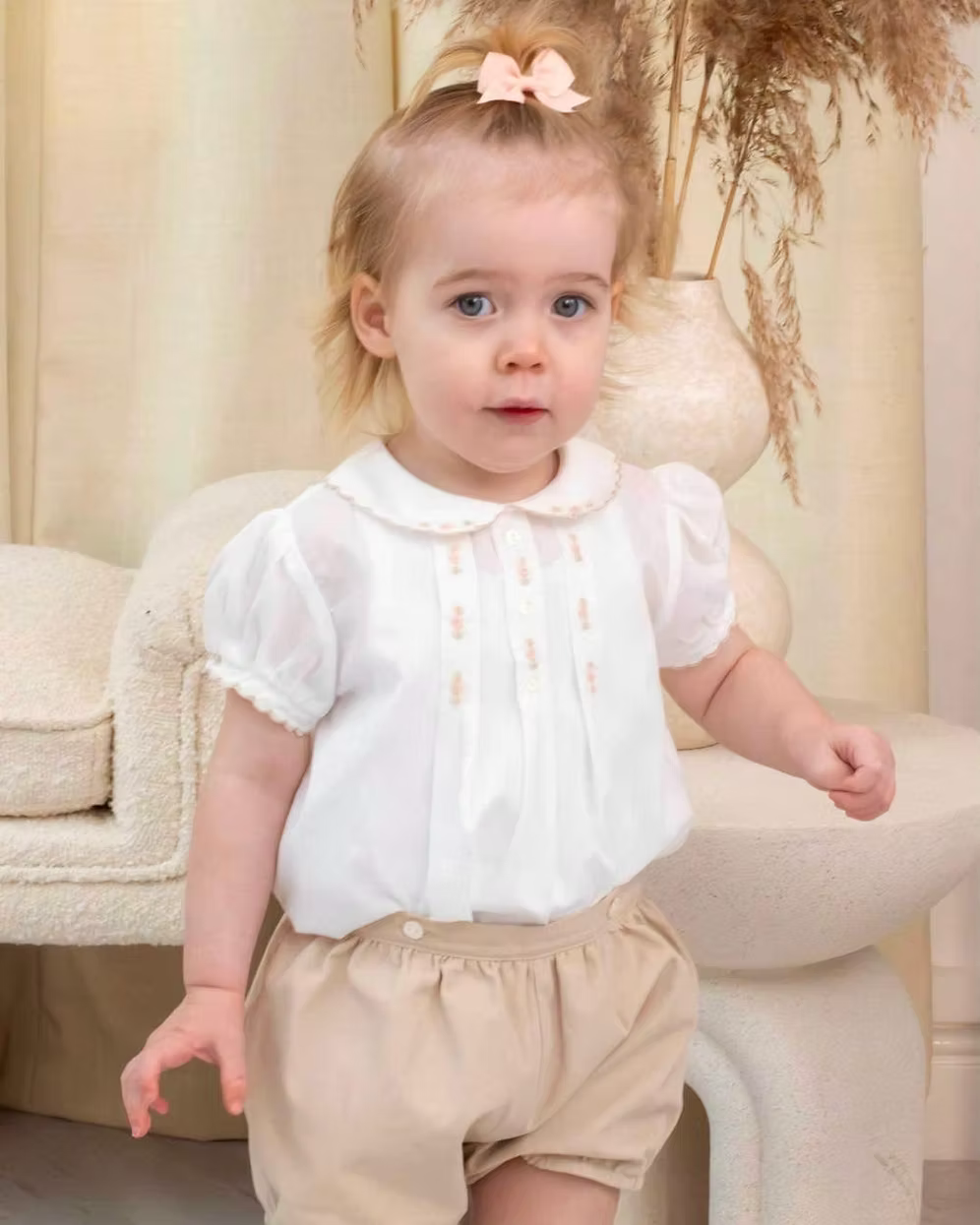 Sarah Louise x Little Lambs Heritage Girls Short Set featuring an ivory hand-smocked blouse with peach embroidery and neutral tailored shorts.
