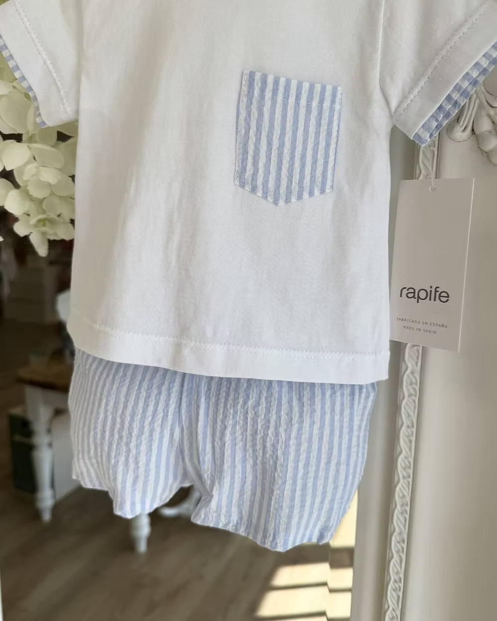 Children's white top with a blue striped pocket and striped shorts hanging on a decorative mirror.