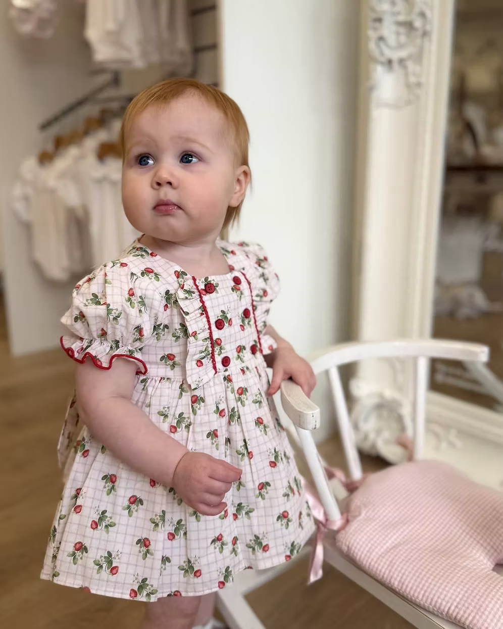 Off-white and pink check baby dress with strawberry print, frill chest detail, puff sleeves, red stitch trims, matching pants, and bow back fastening.