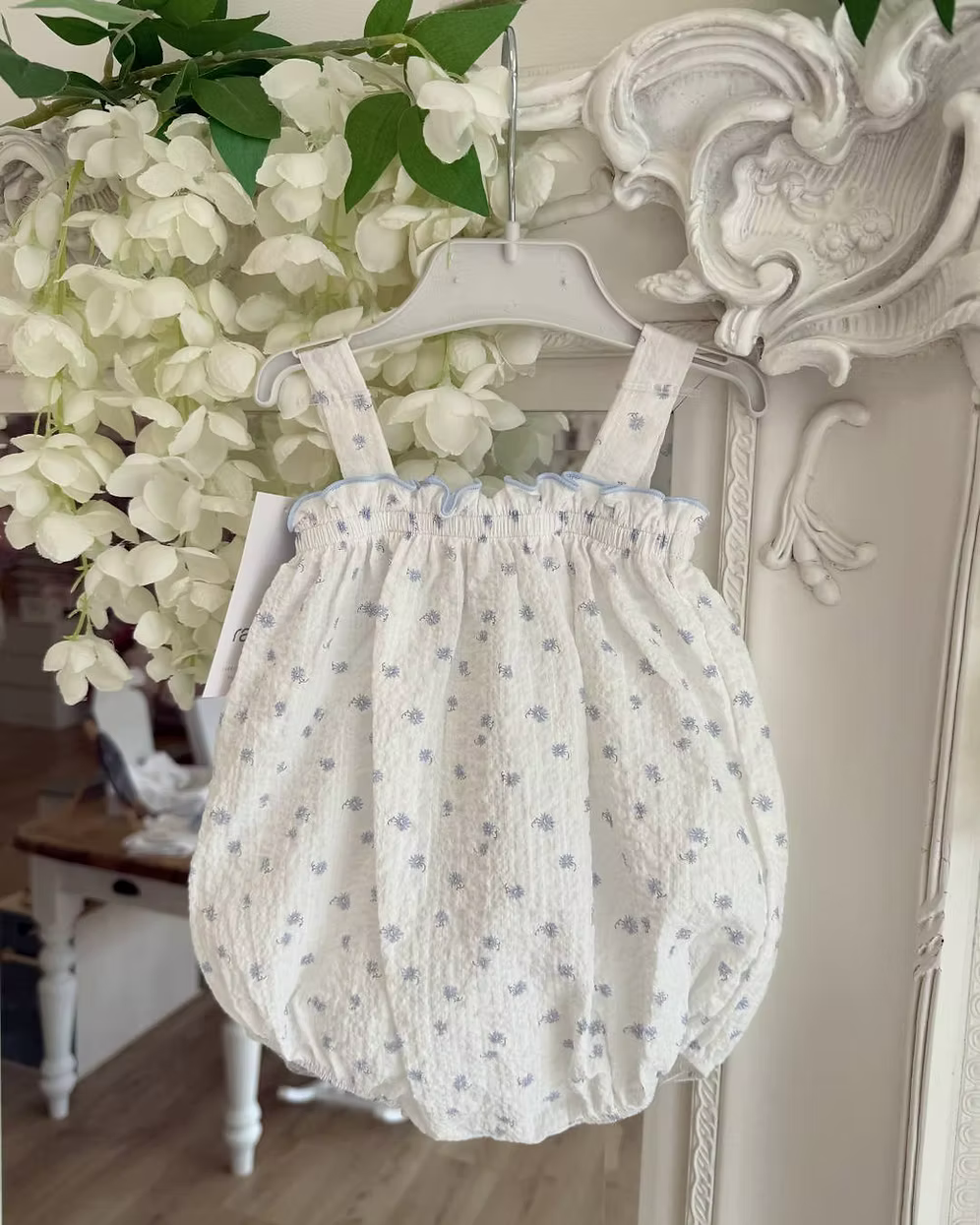 Blue Flower Romper. Designed in a soft white crinkle-textured fabric, this delicate piece is adorned with dainty blue floral detailing
