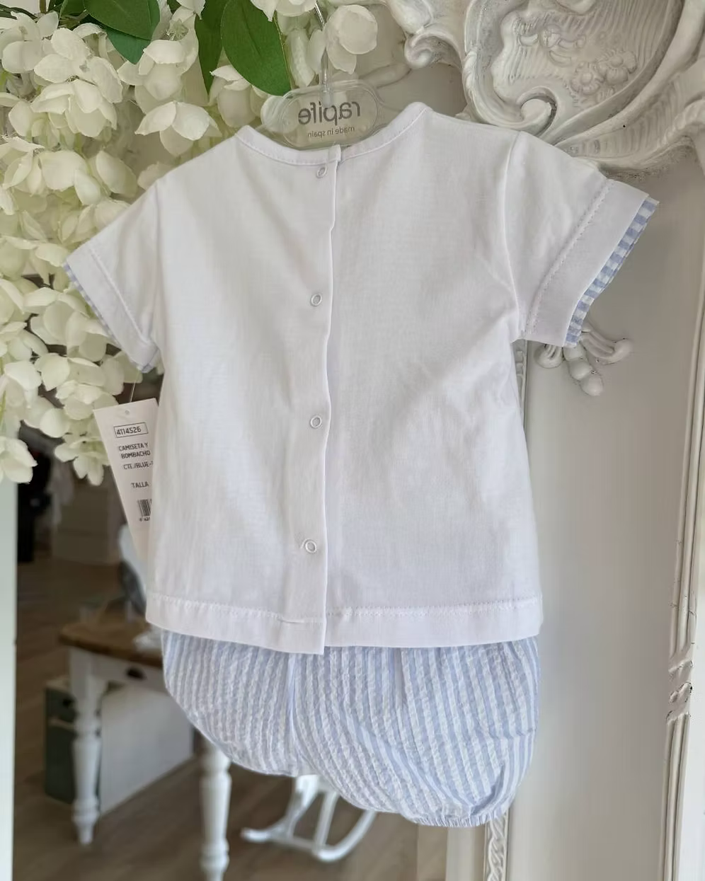 Children's white shirt with aback popper fastening and striped shorts hanging on a decorative mirror.