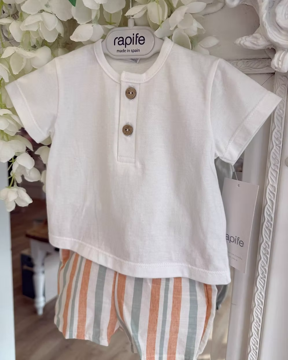 featuring striped shorts in soft off-white with pops of green and orange. Paired perfectly with a crisp white tee, finished with a simple wooden button neckline