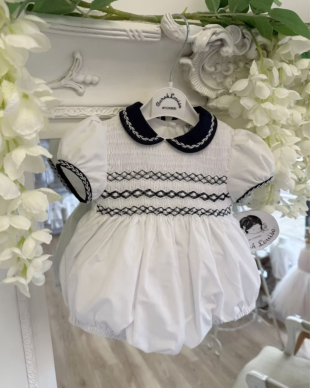 Baby girls white bubble romper with navy Peter Pan collar, sleeve trim and full smocked chest