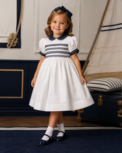 Young girl in a white dress with navy details standing in a nautical-themed room.