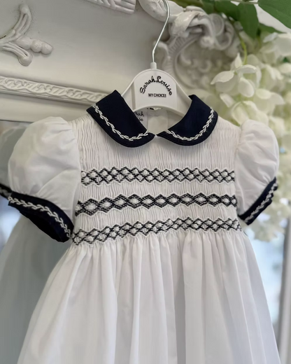 White dress with navy trim on a hanger against a decorative white background