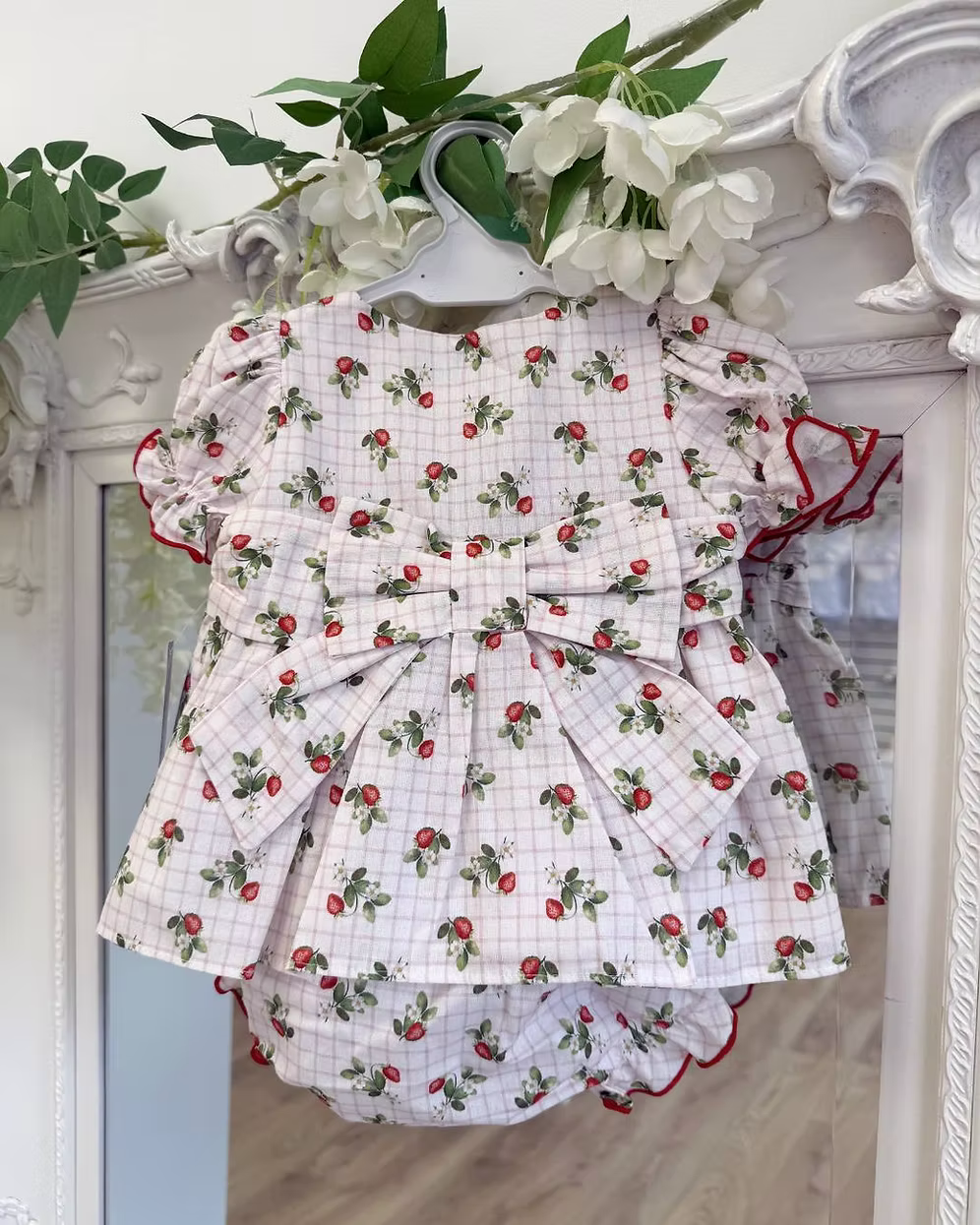 Off-white and pink check baby dress with strawberry print, frill chest detail, puff sleeves, red stitch trims, matching pants, and bow back fastening.