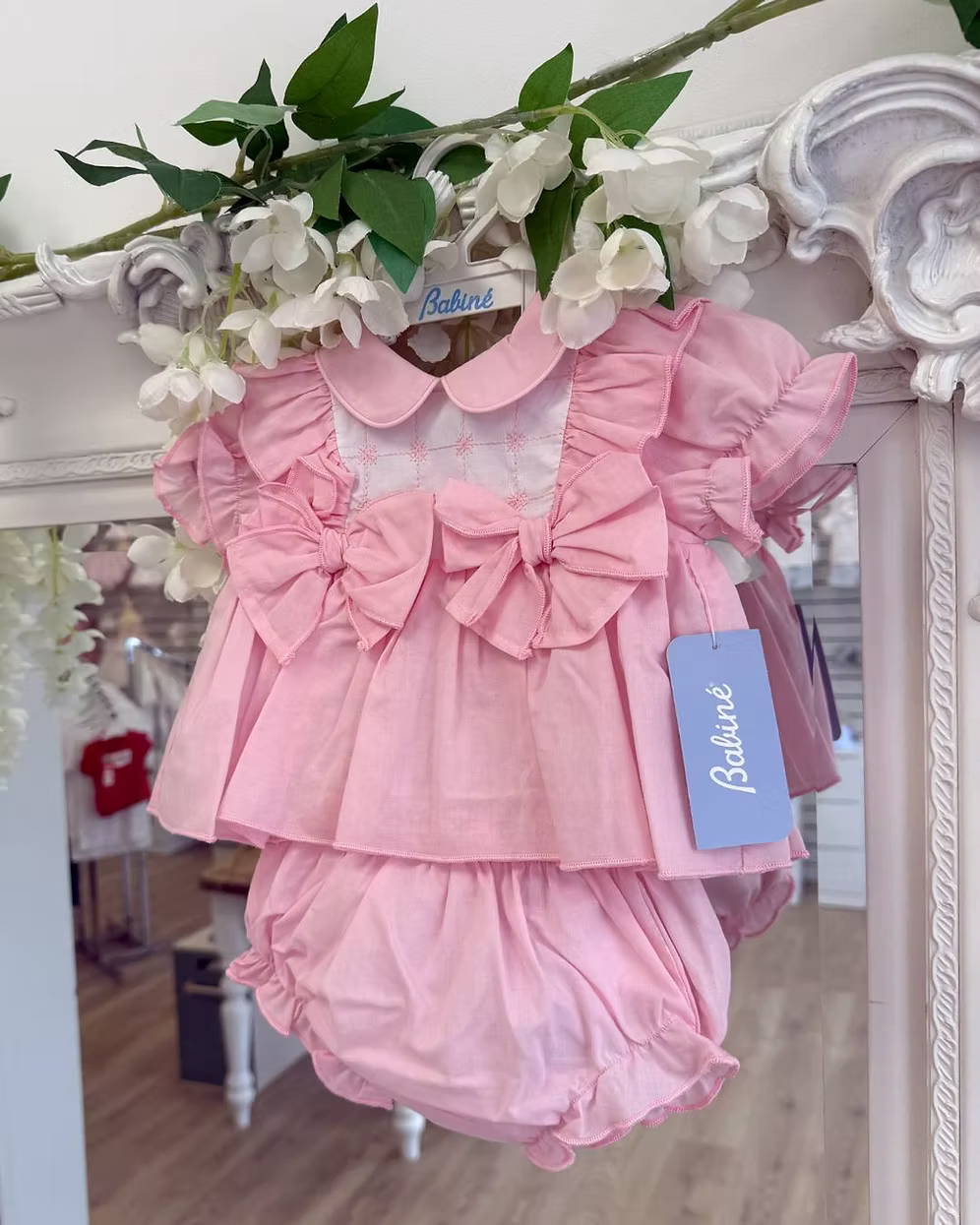 A soft rosy pink, this traditional Spanish-style dress is paired with matching jam pants. Adorned with a white chest panel featuring subtle stitch detailing, the dress is finished with pretty shoulder frills, two bow accents and a classic Peter Pan collar.