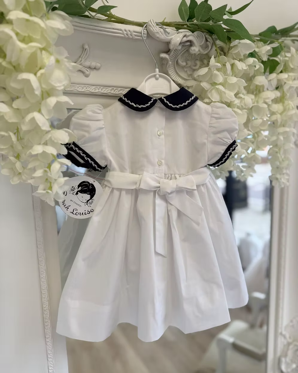 White dress with navy trim on a hanger against a decorative floral background