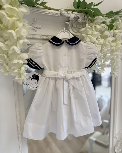 White dress with navy trim on a hanger against a decorative floral background